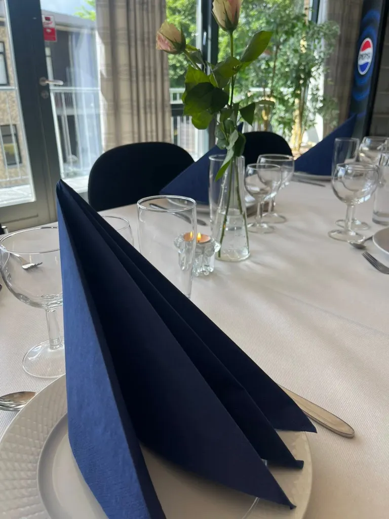 Kuvert med blå serviet, glas og en rose på et dækket bord